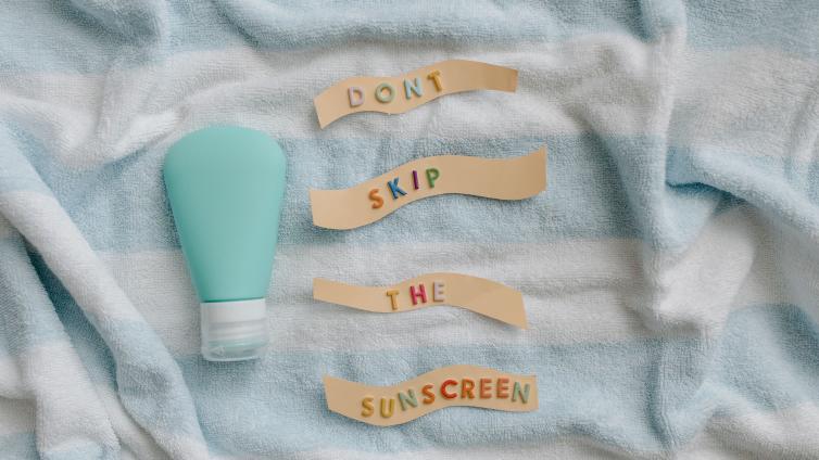 Flat lay of sunscreen bottle with message 'Don't skip the sunscreen' on a towel